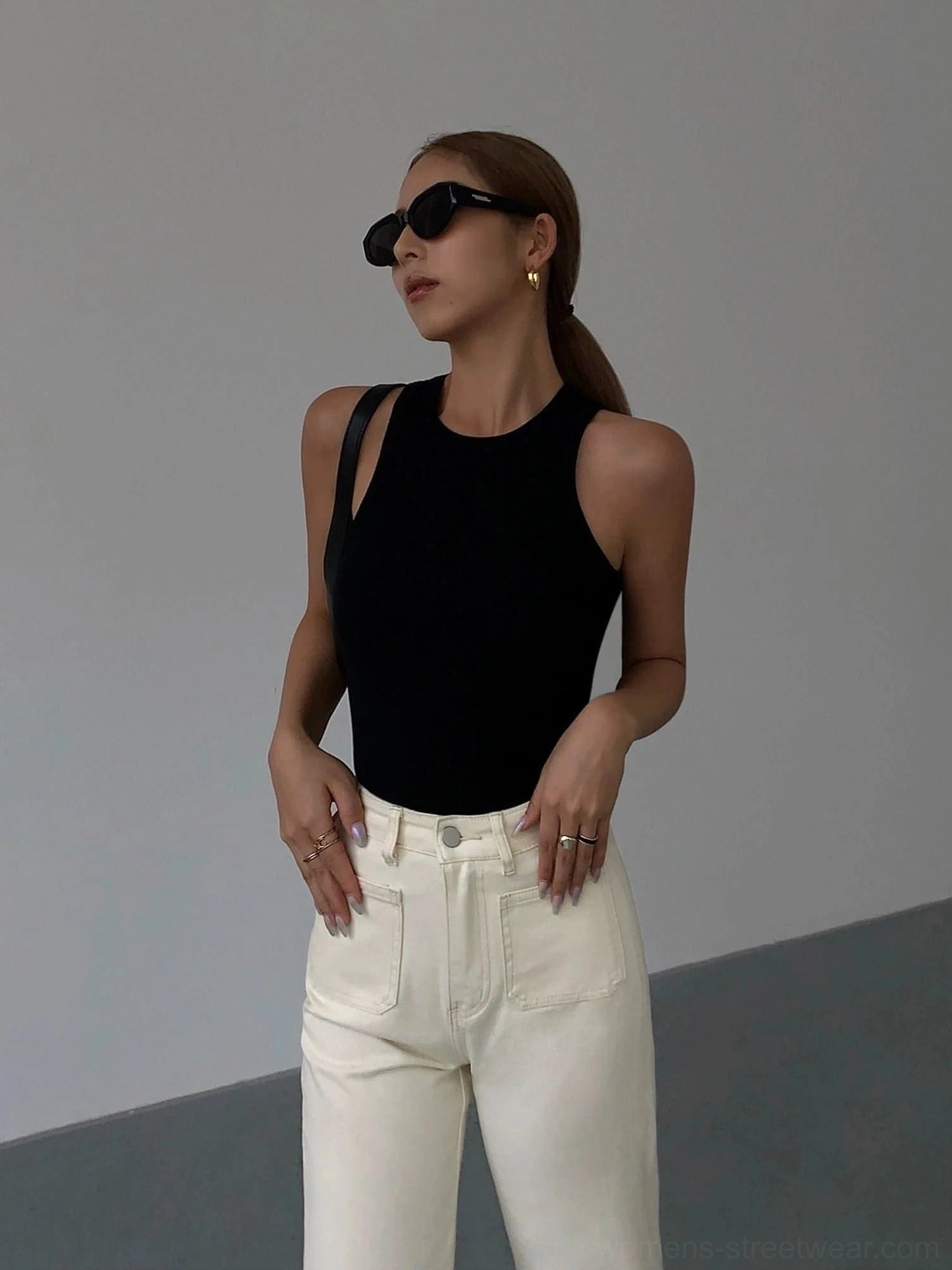 Black ribbed knit tank top front half-body view on female model with black sunglasses, paired with off-white straight leg jeans, minimalist aesthetic