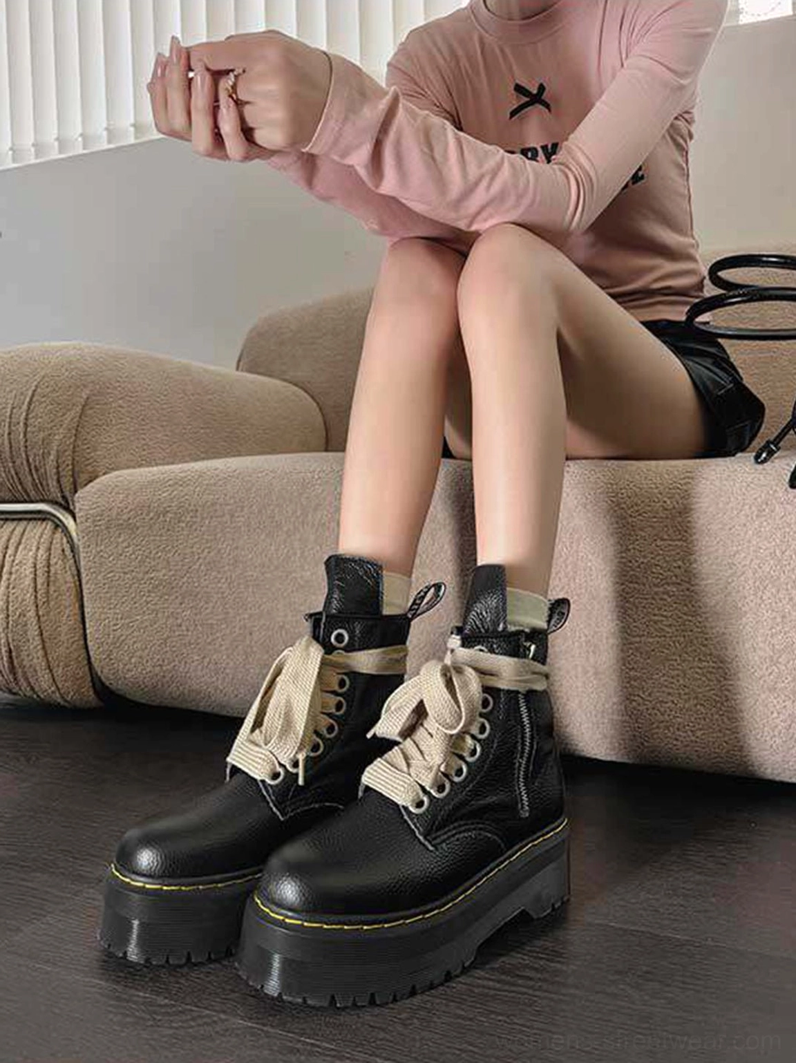Black ribbon-laced combat boots with thick platform outsoles and yellow stitching styled with black shorts and a pink top