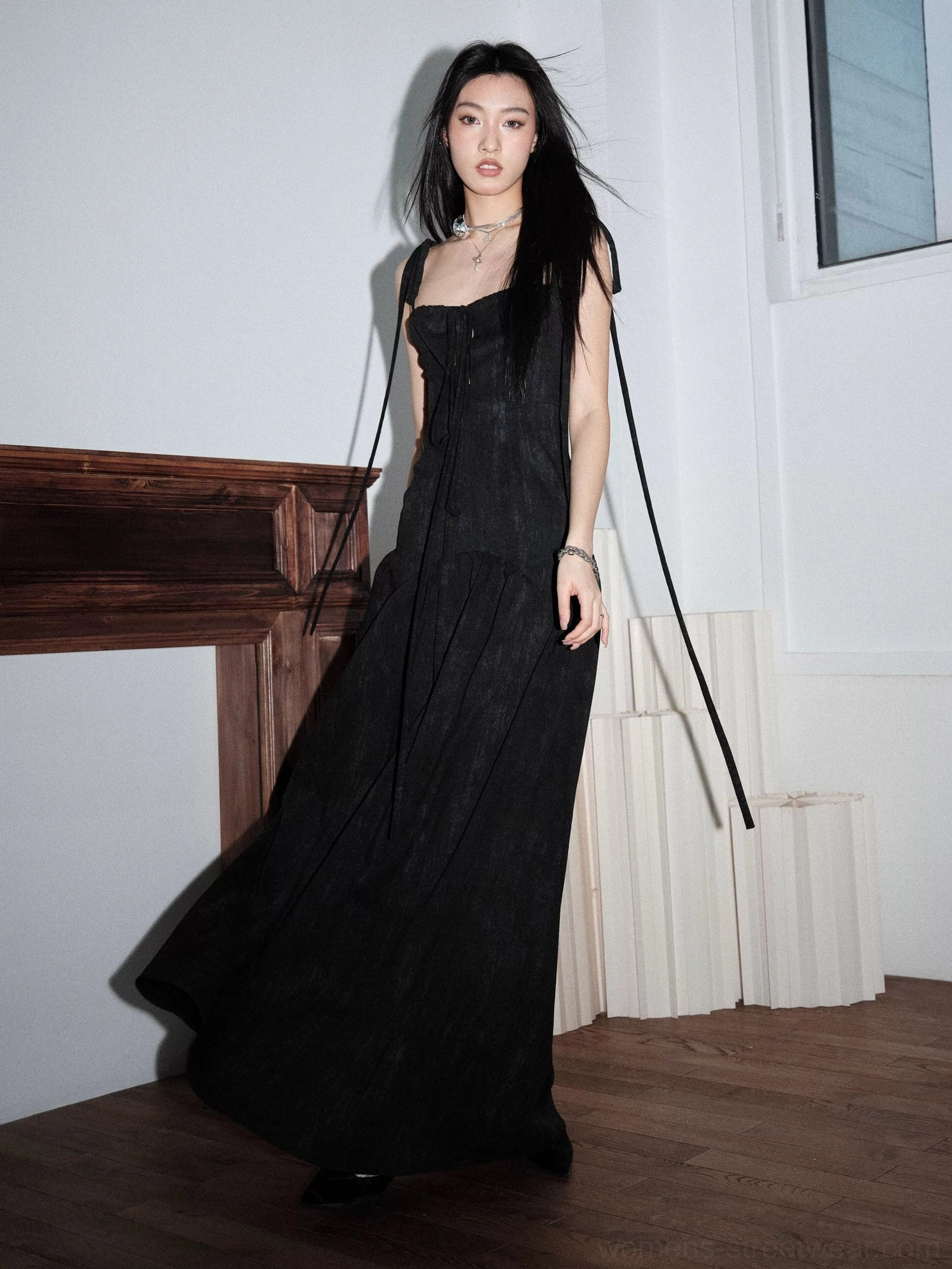 Rear side view of a black ribbon-strap maxi dress with long trailing shoulder ties, matte textured fabric, and flowing floor-length skirt