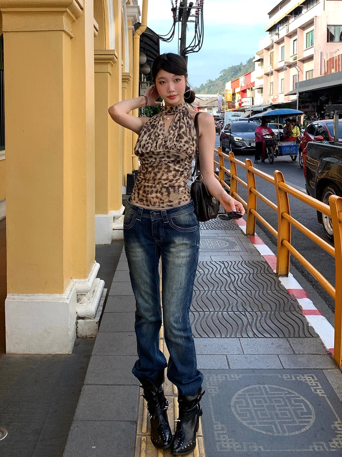 Black rivet buckle pointed-toe ankle boots worn with leopard halter top and wide-leg jeans on an urban street