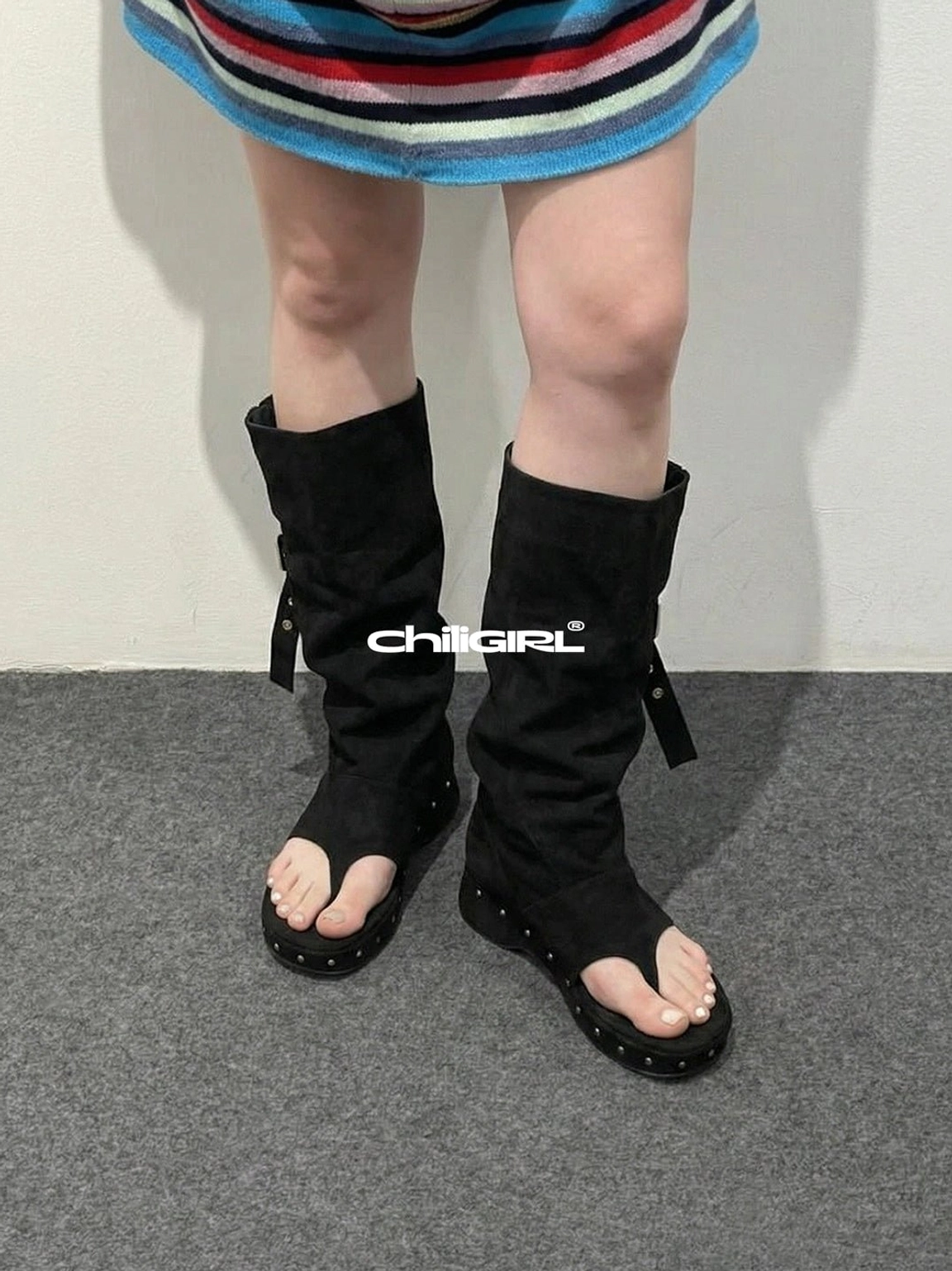 Black rivet thong low-wedge mid-calf sandal boots paired with striped knit top and mini skirt in Y2K streetwear look