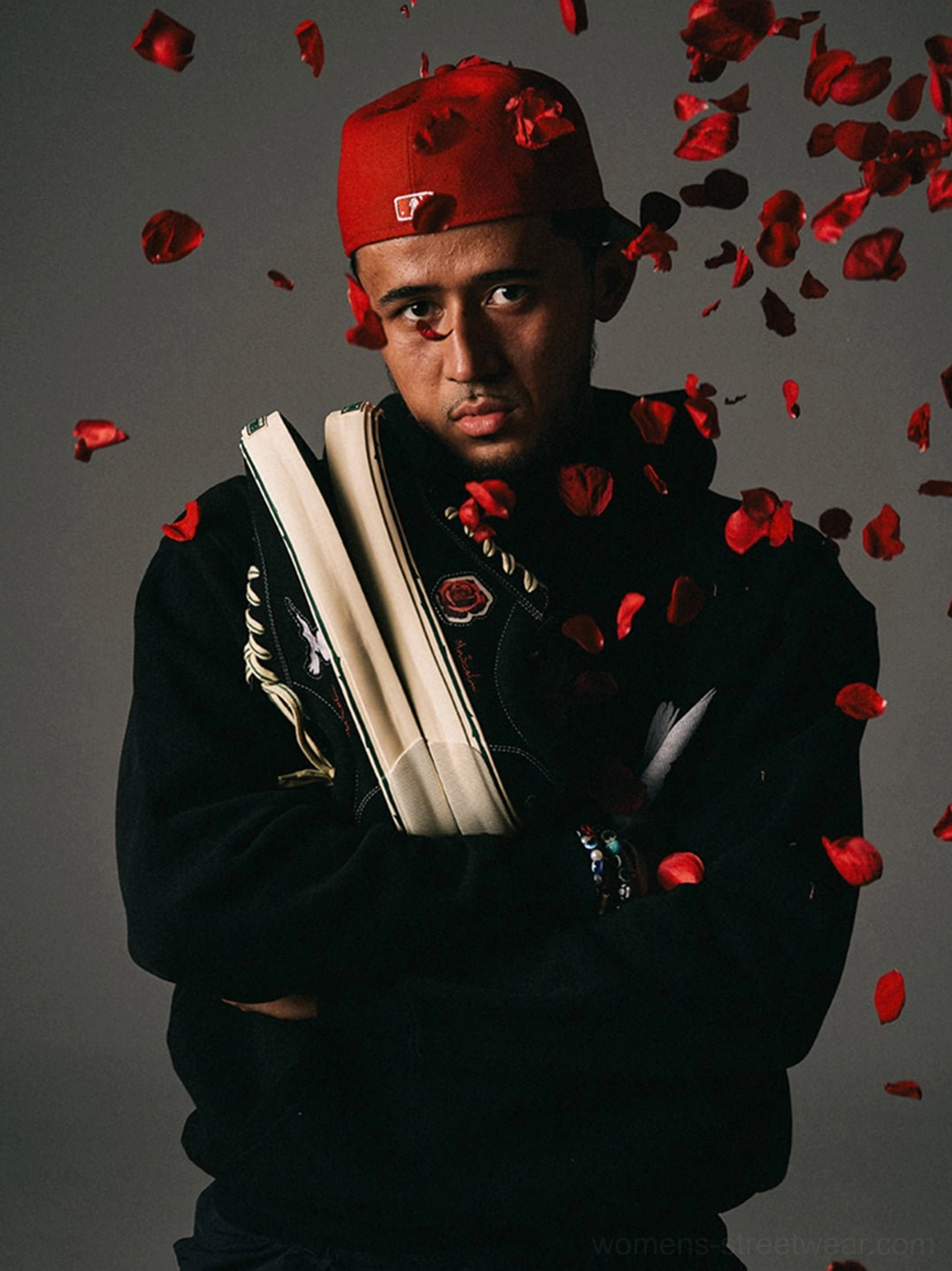 Black embroidered low-top skate shoes presented with a red bandana and falling rose petals in an editorial streetwear scene