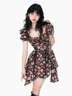 Front three-quarter view of a black rose floral puff-sleeve mini dress with square neckline, waist tie, fitted bodice, and asymmetric handkerchief hem