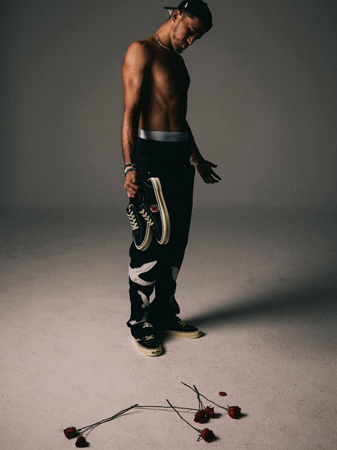 Full-body streetwear styling featuring black rose embroidered low-top skate shoes and rose accents on the studio floor