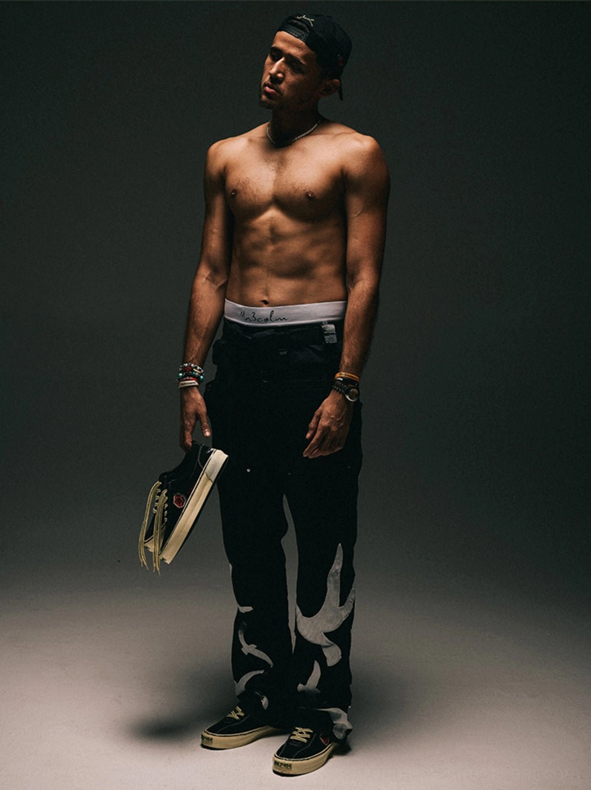 Streetwear fashion model holding black rose embroidered low-top skate shoes with graphic trousers in a studio setting