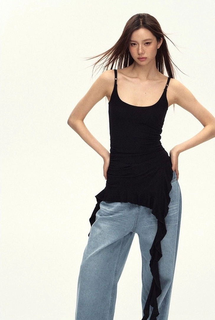 Back three-quarter view of a black ruched cami top with spaghetti straps and uneven ruffled hem styled for streetwear