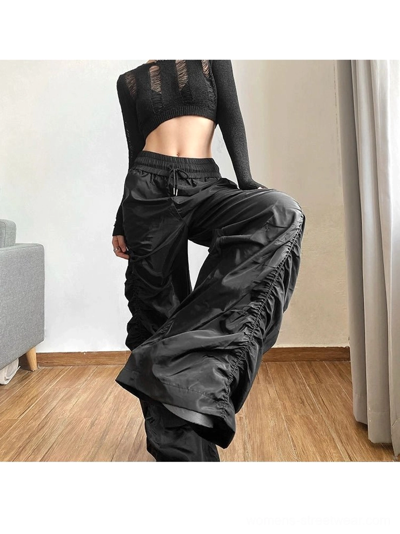 Black ruched wide-leg streetwear pants shown in a relaxed seated side view with a cropped long-sleeve top