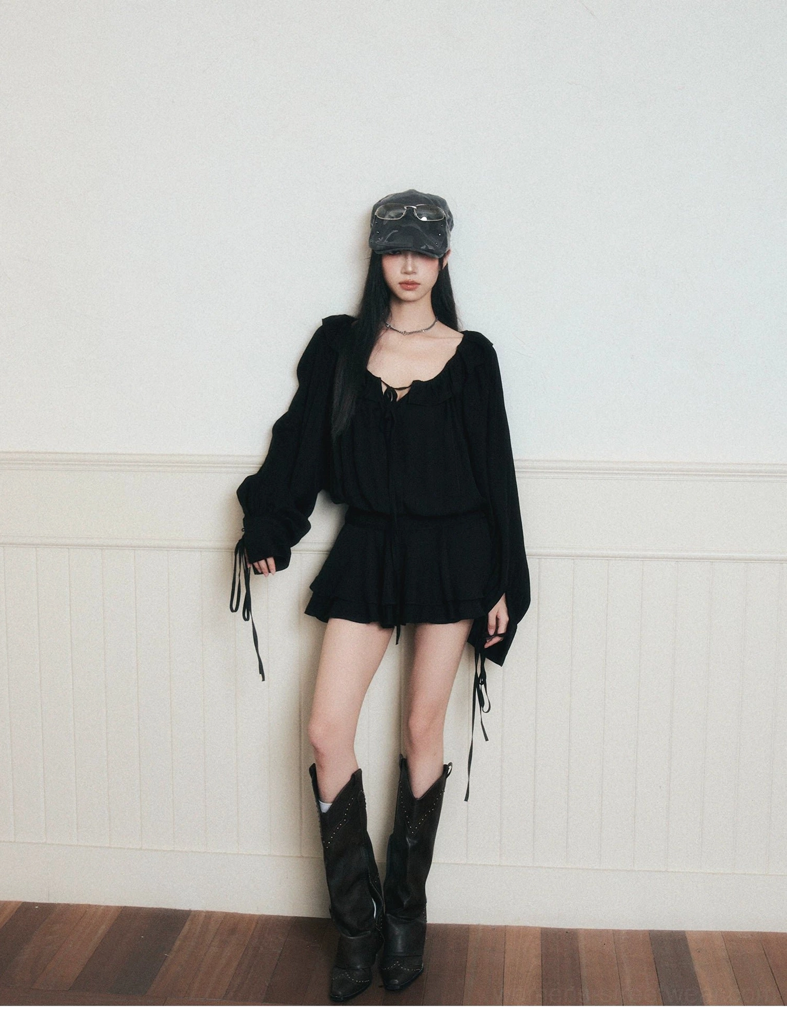 Black ruffle poet mini dress set styled with gray newsboy cap and black western boots in a vintage studio