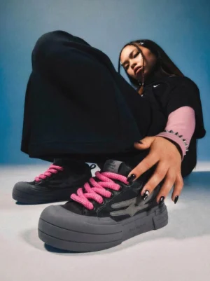 Black pink-accented platform sneakers styled with all-black streetwear in a low-angle indoor fashion shot