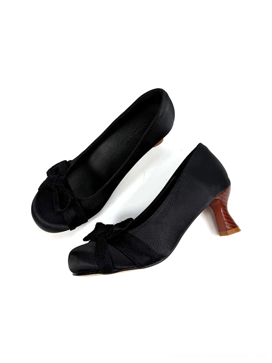 Black satin bow pumps displayed from the right oblique angle with sleek upper, wood-look heel grain, and romantic styling