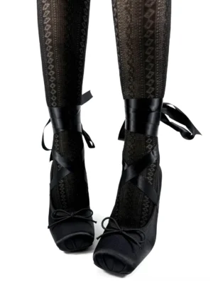 Black satin bow strap pumps worn with patterned sheer tights, showing the square toe, ankle ribbons, and heart buckle detail
