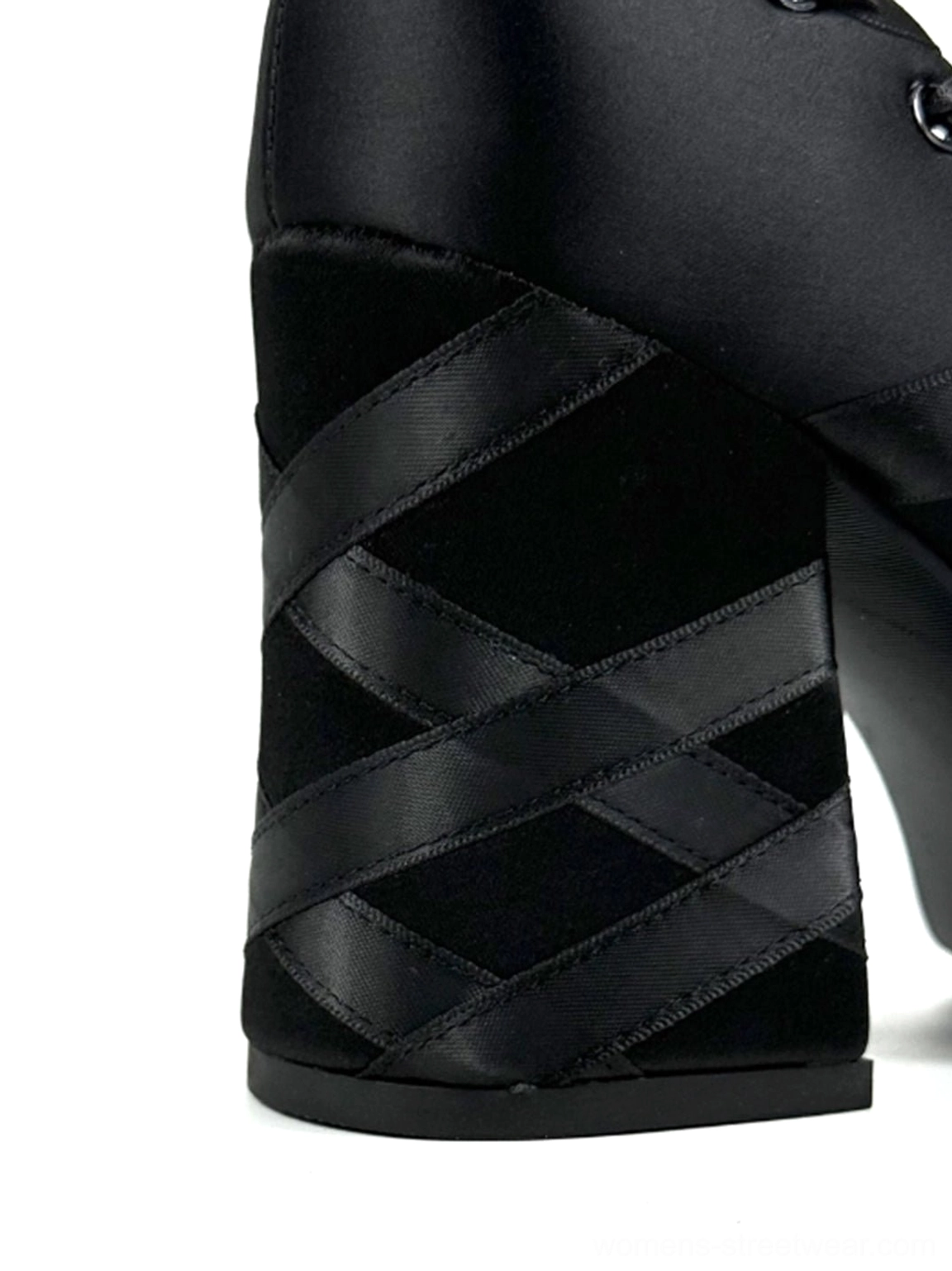 Close-up side view of black satin platform pump heel with crisscross ribbon decoration, matte satin upper, and chunky block heel