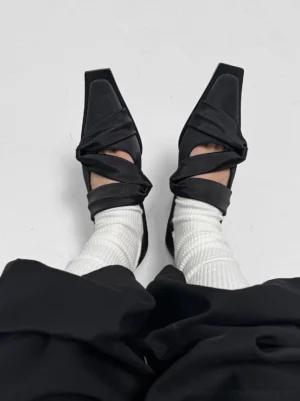 Woman wearing black satin square-toe ballet flats with white ribbed socks and black wide-leg trousers in a modern Seoul streetwear outfit