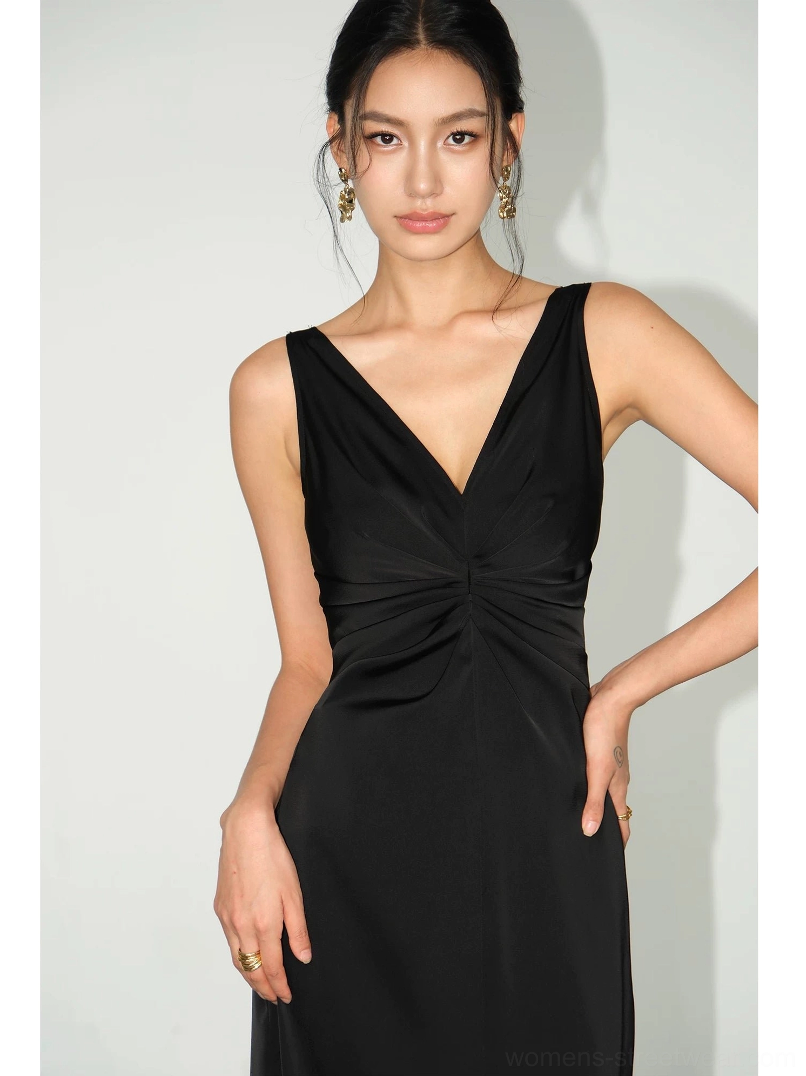 Black satin twist-front maxi dress close-up showing deep V-neckline, gathered bust ruching, sleeveless slim fit and smooth glossy fabric