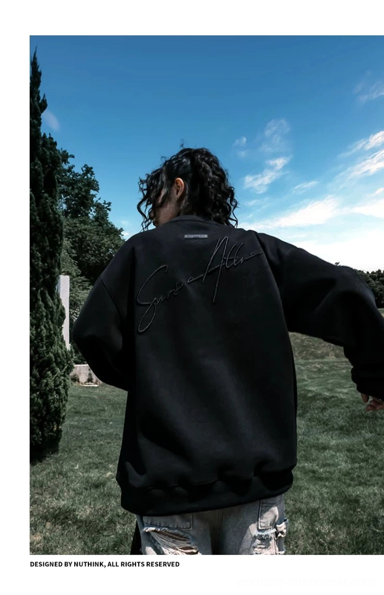 Rear view of a model wearing a black oversized script embroidered crewneck sweatshirt with ripped denim shorts and casual streetwear styling