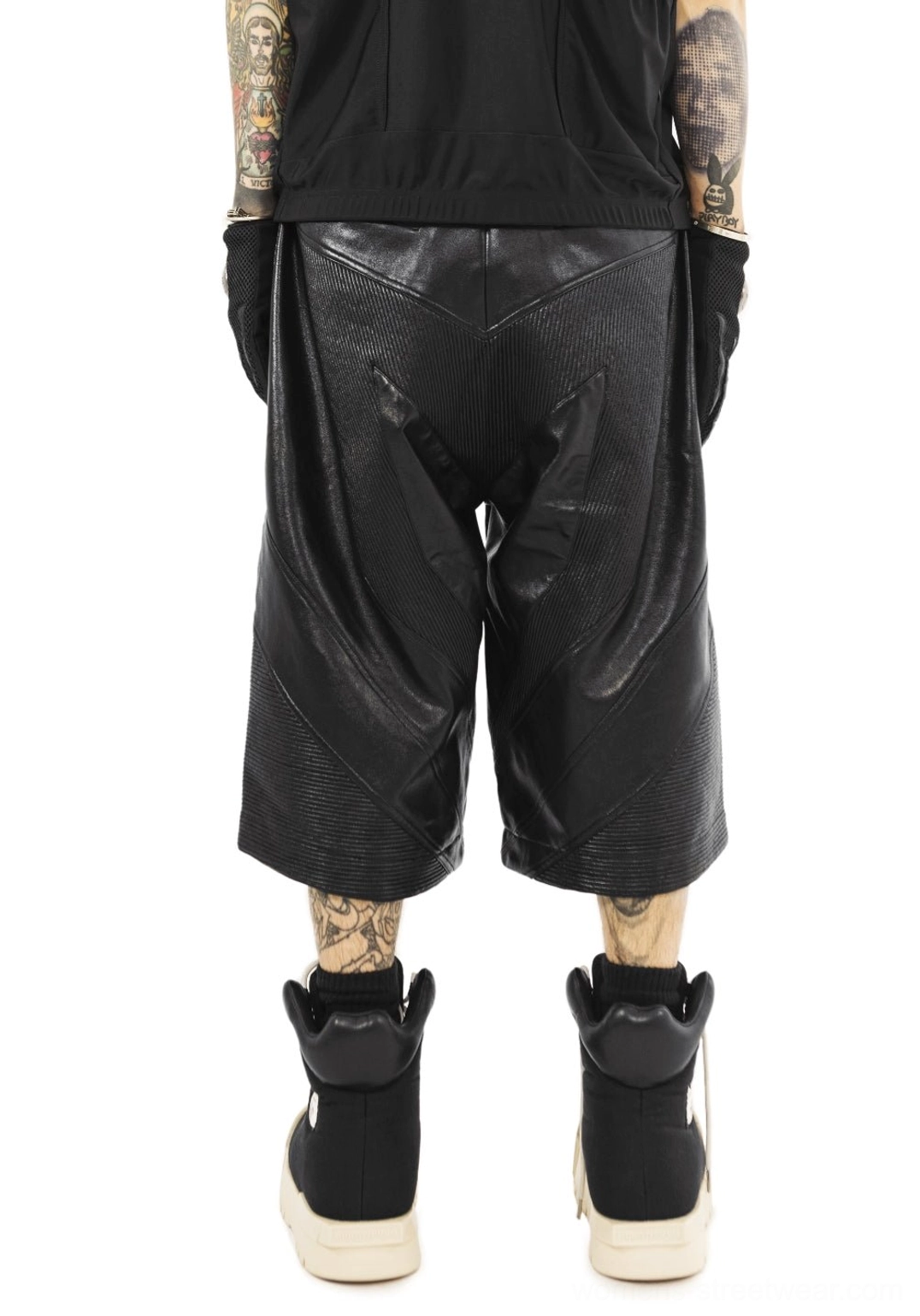 Full rear outfit view featuring black sculpted-toe platform boots styled with cropped black leather pants, black socks, and a monochrome streetwear look