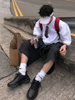 Black sculpted-sole chunky sneakers worn with white crew socks in an urban preppy streetwear outfit beside a city curb