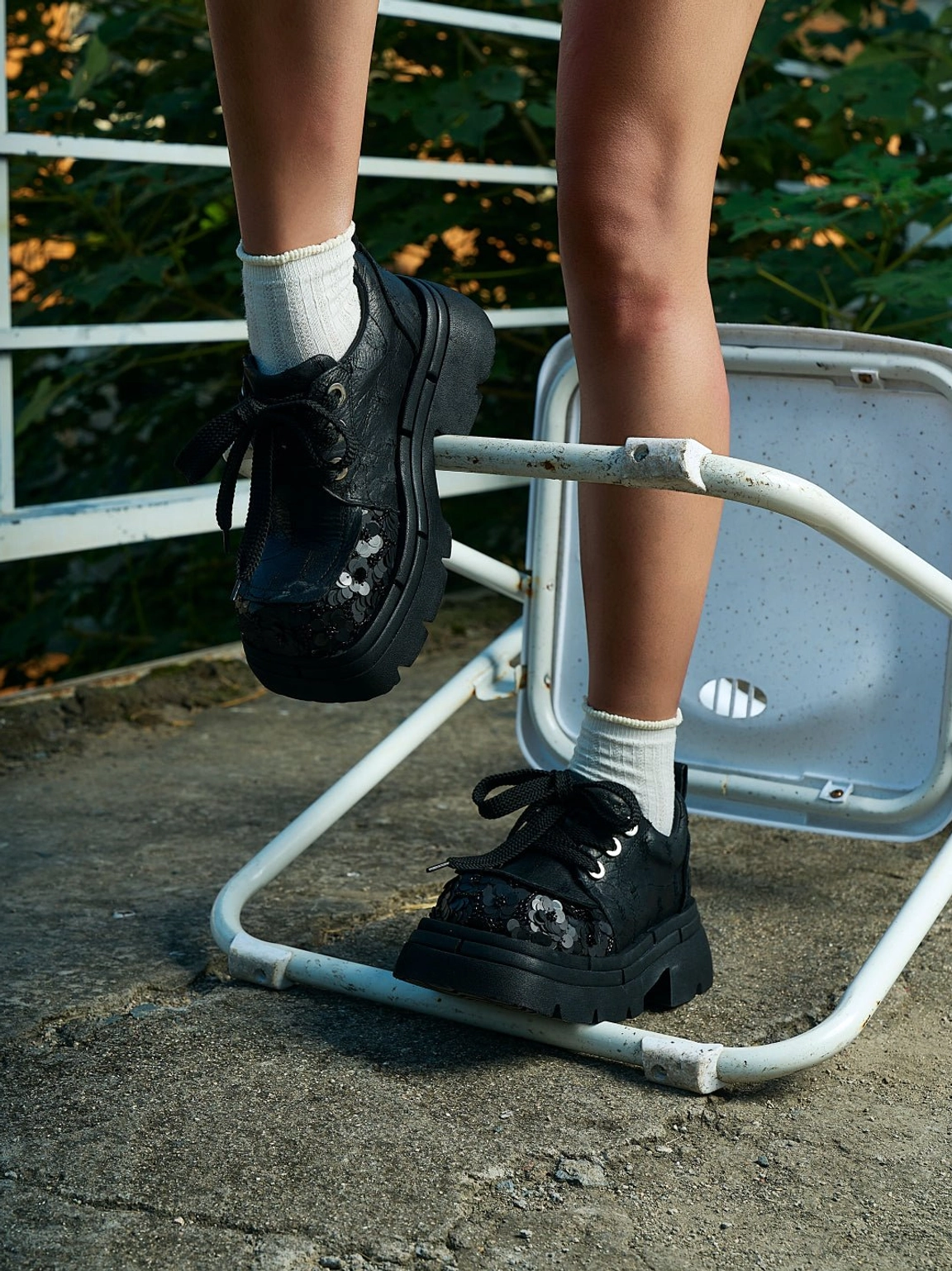 Black sequined platform derby shoes styled with white crew socks on a model outdoors, showing chunky streetwear soles and decorative floral toe caps