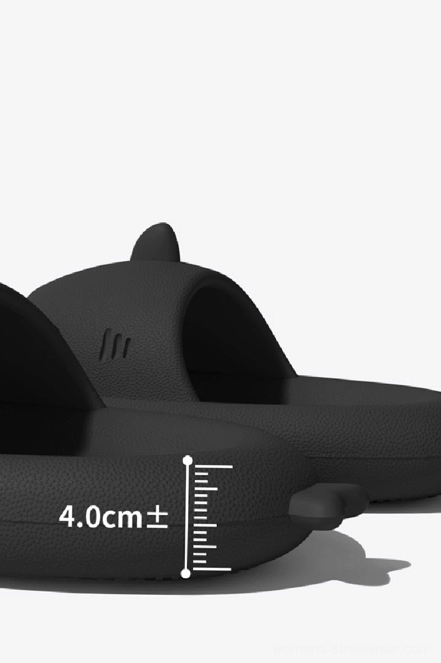 Black shark slide slippers shown from the side with a 4cm thick cushioned sole, shark fin, and tooth details