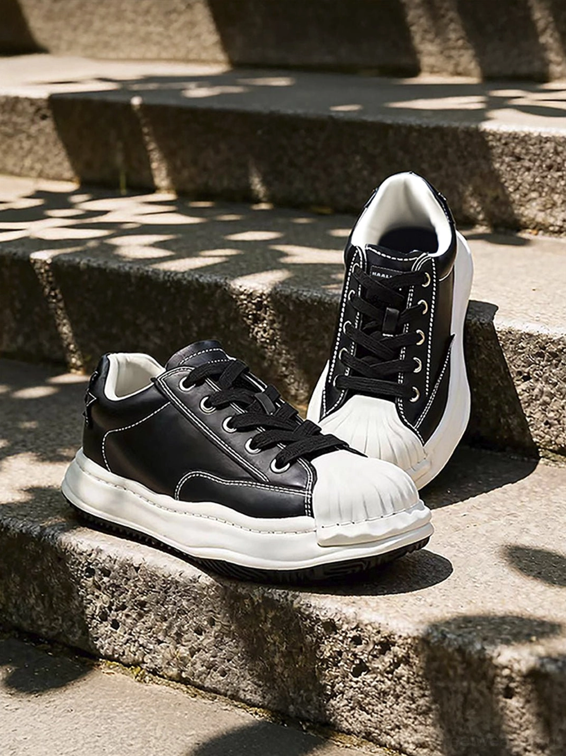 Black shell-toe casual sneakers shown on sunlit stone stairs with matte upper, white sole, and subtle star heel detail