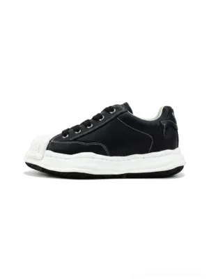 Black shell-toe court sneakers in a side frontal product view with matte synthetic-leather upper, molded white toe cap, thick white sole, and black lace-up design