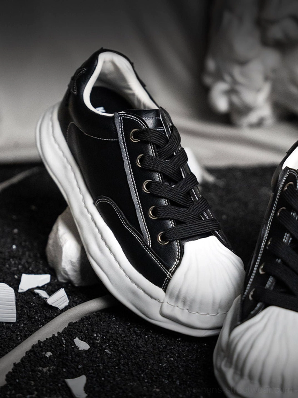 Black shell-toe court sneakers with a molded white toe and chunky white sole styled as modern unisex streetwear footwear