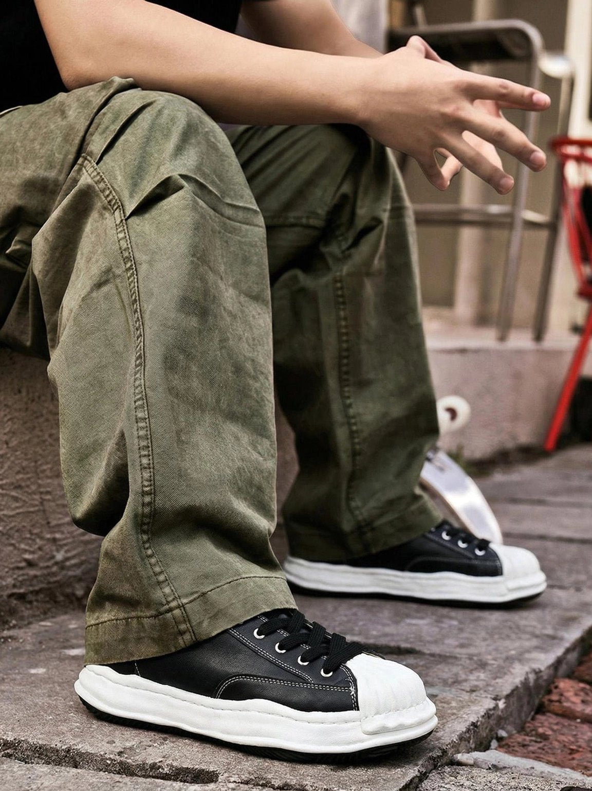Side view of black shell-toe court sneakers worn with olive cargo pants, highlighting the low-top cut and oversized white rubber sole