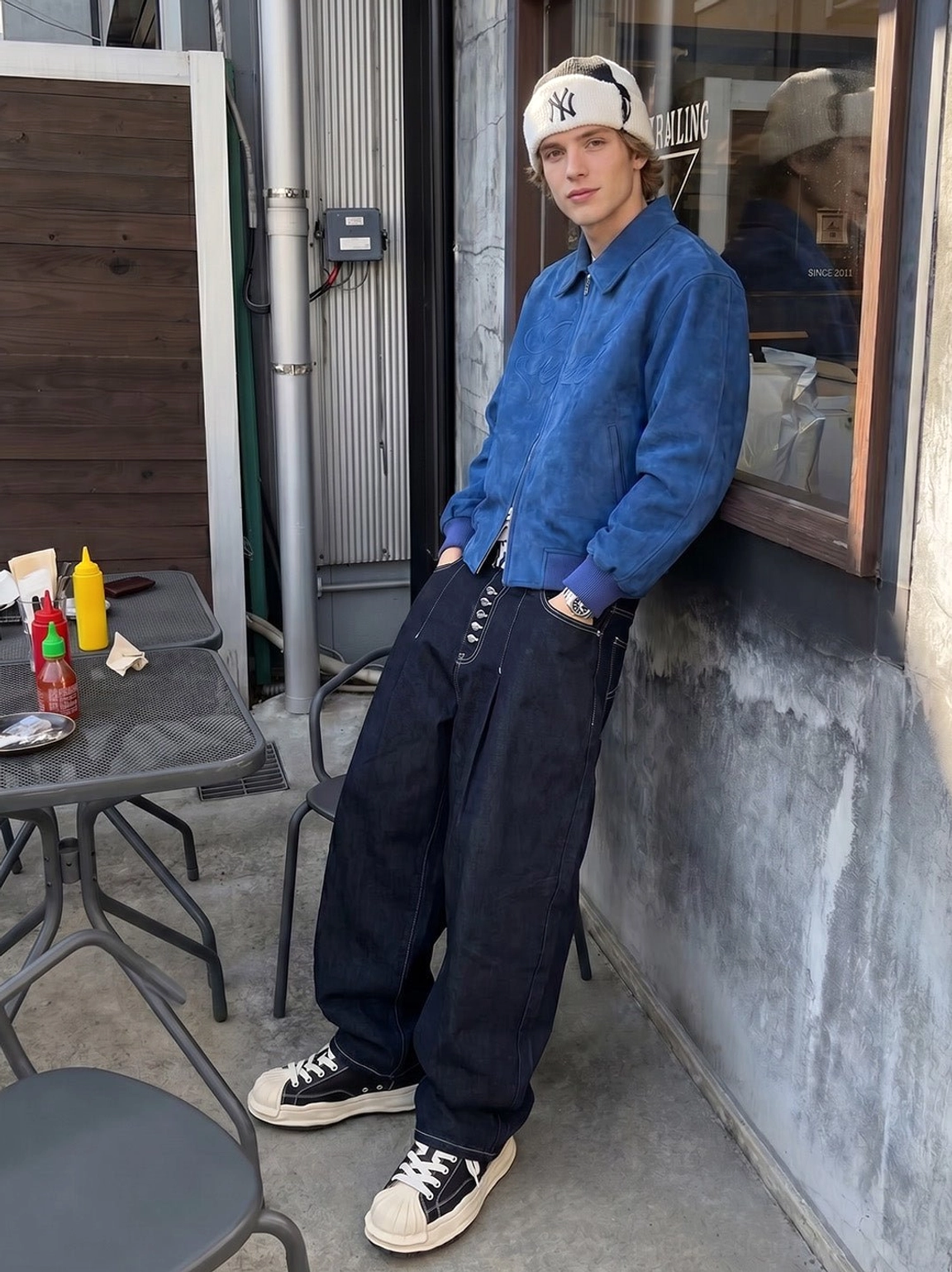 Unisex black shell-toe platform sneakers worn with a blue shirt and wide-leg jeans in a relaxed Seoul-inspired street style look
