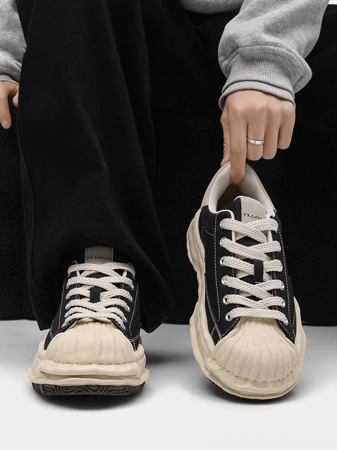 Flat lay showing front and side views of black shell-toe platform sneakers with a cream rubber toe and thick elevated sole