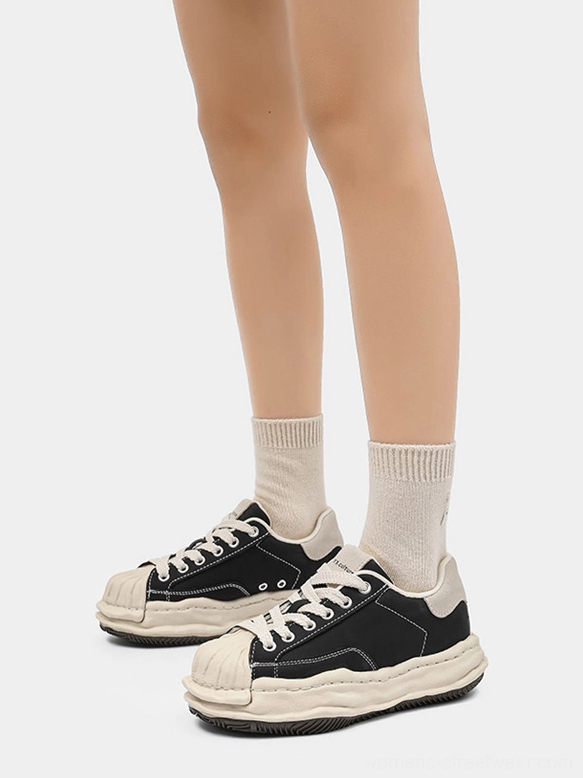 Front view of black shell-toe platform sneakers worn with beige crew socks highlighting the contrasting cream toe design