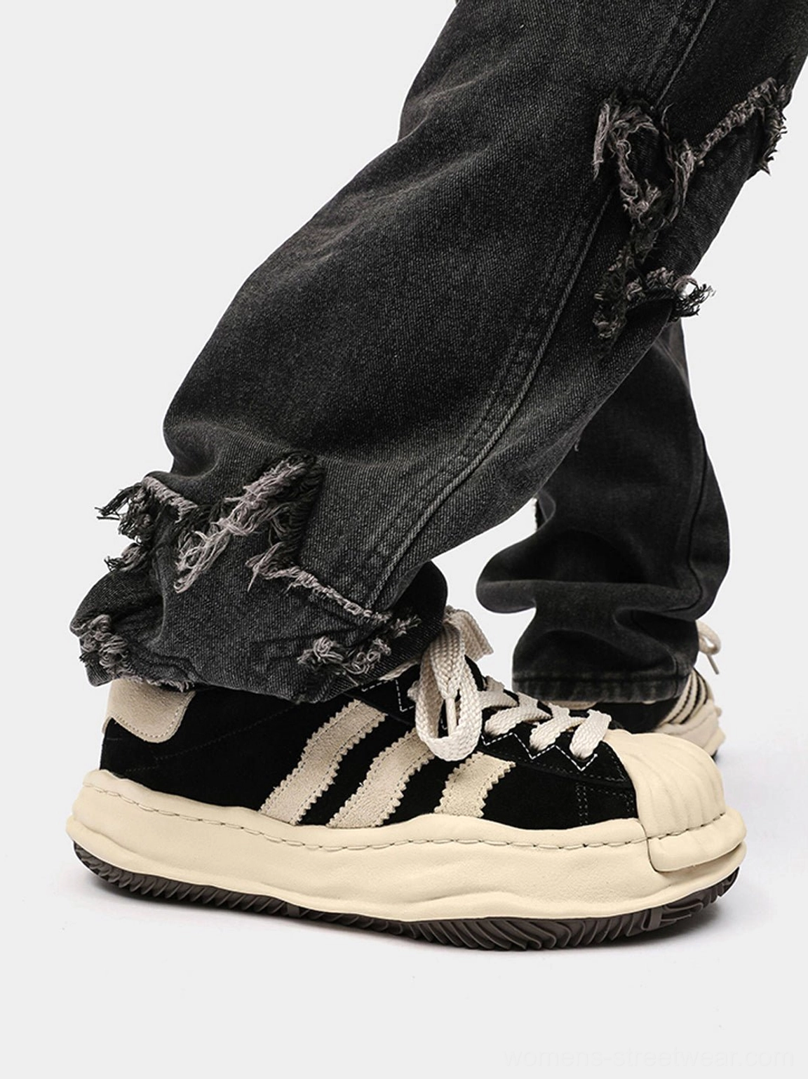 Rear side view of black melted shell-toe platform sneakers worn with frayed dark denim, showing the heel counter and textured outsole