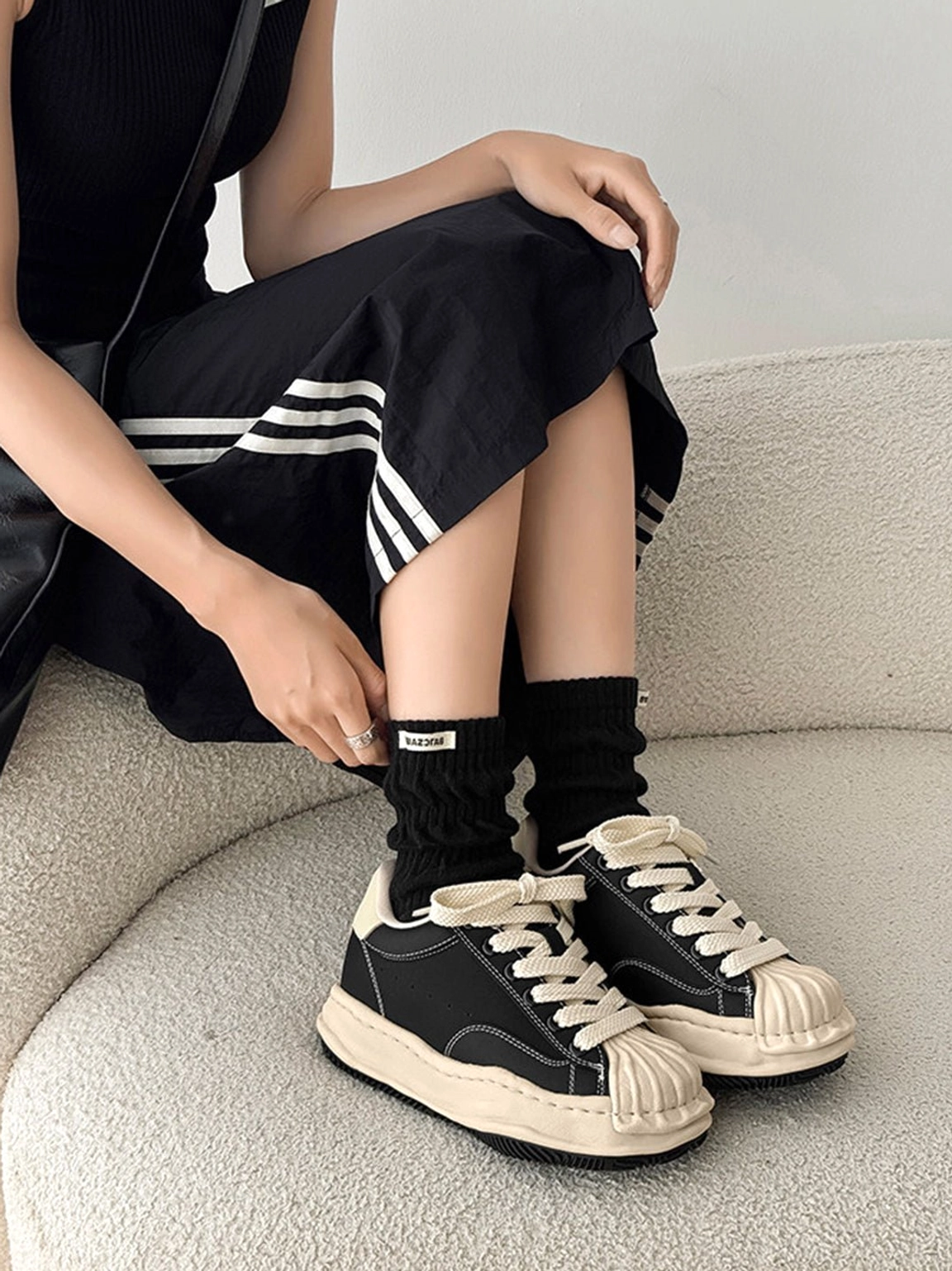 Black distressed shell-toe platform sneakers worn with a ribbed top, striped skirt, and casual streetwear styling