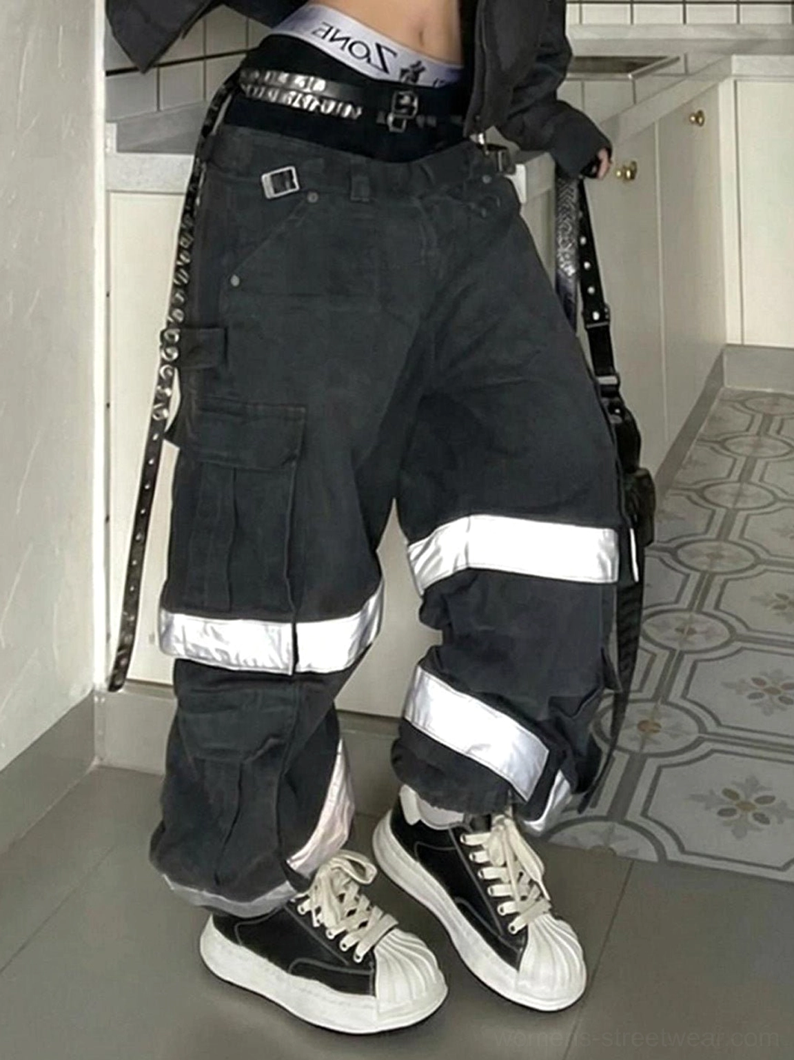 Black low-top shell-toe sneakers styled with reflective stripe cargo pants, black laces, and a clean minimalist court sneaker silhouette