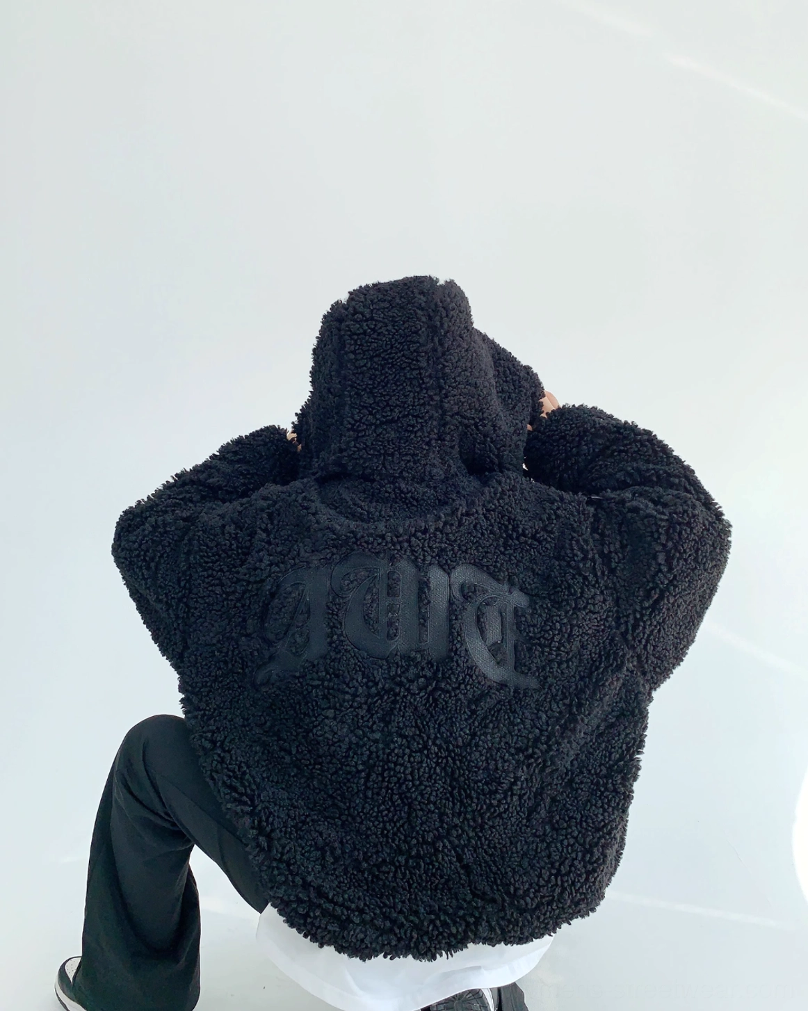 Low-angle back view of black sherpa teddy zip hoodie displaying gothic back lettering, oversized hood, plush fleece, and loose avant-garde streetwear cut