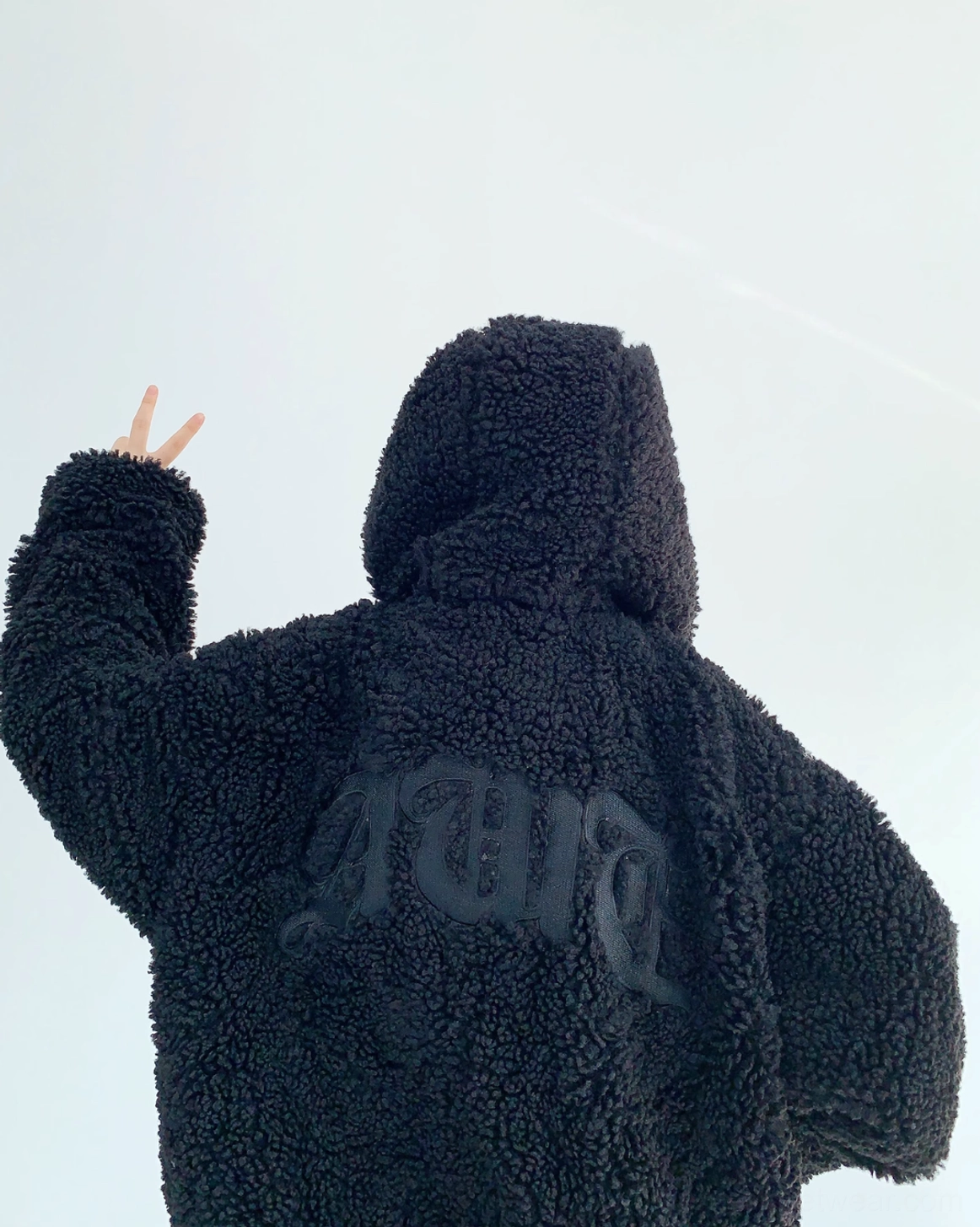 Back view of black oversized sherpa zip hoodie showing gothic lettering, plush teddy fleece texture, attached hood, and relaxed streetwear fit