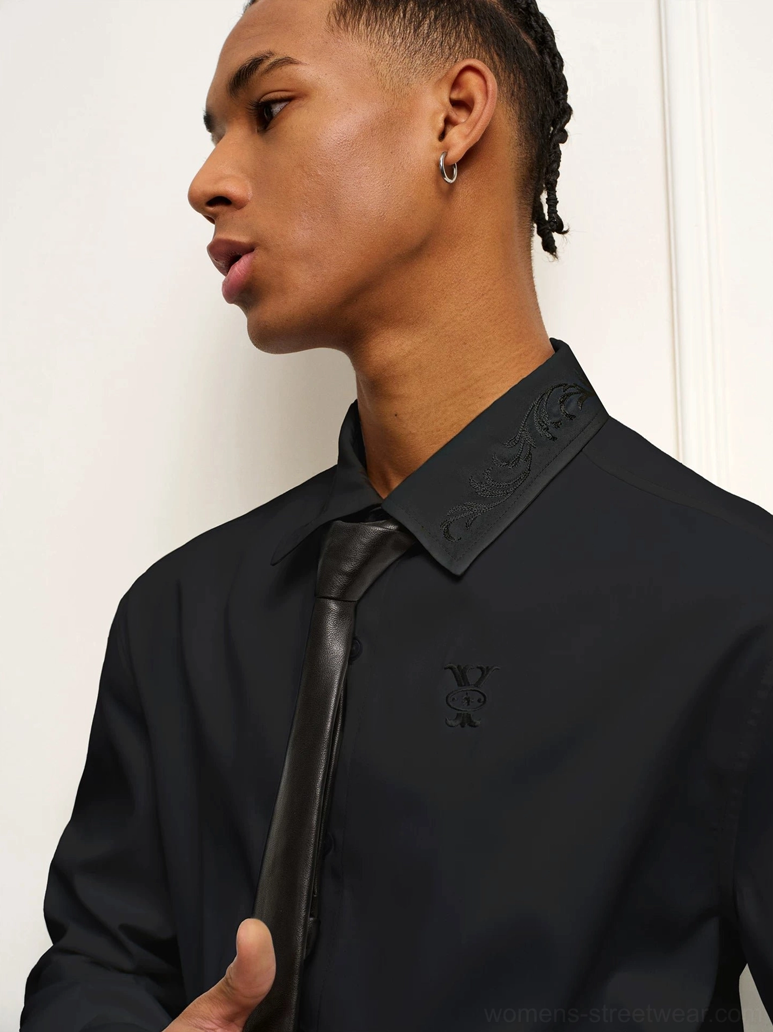Close-up of black shirt point collar with baroque embroidery, subtle chest detail, and black necktie