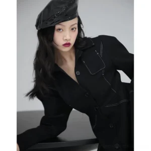 Close-up view of black shirt dress with white contrast topstitching, structured collar, button fastening, and chest flap pocket