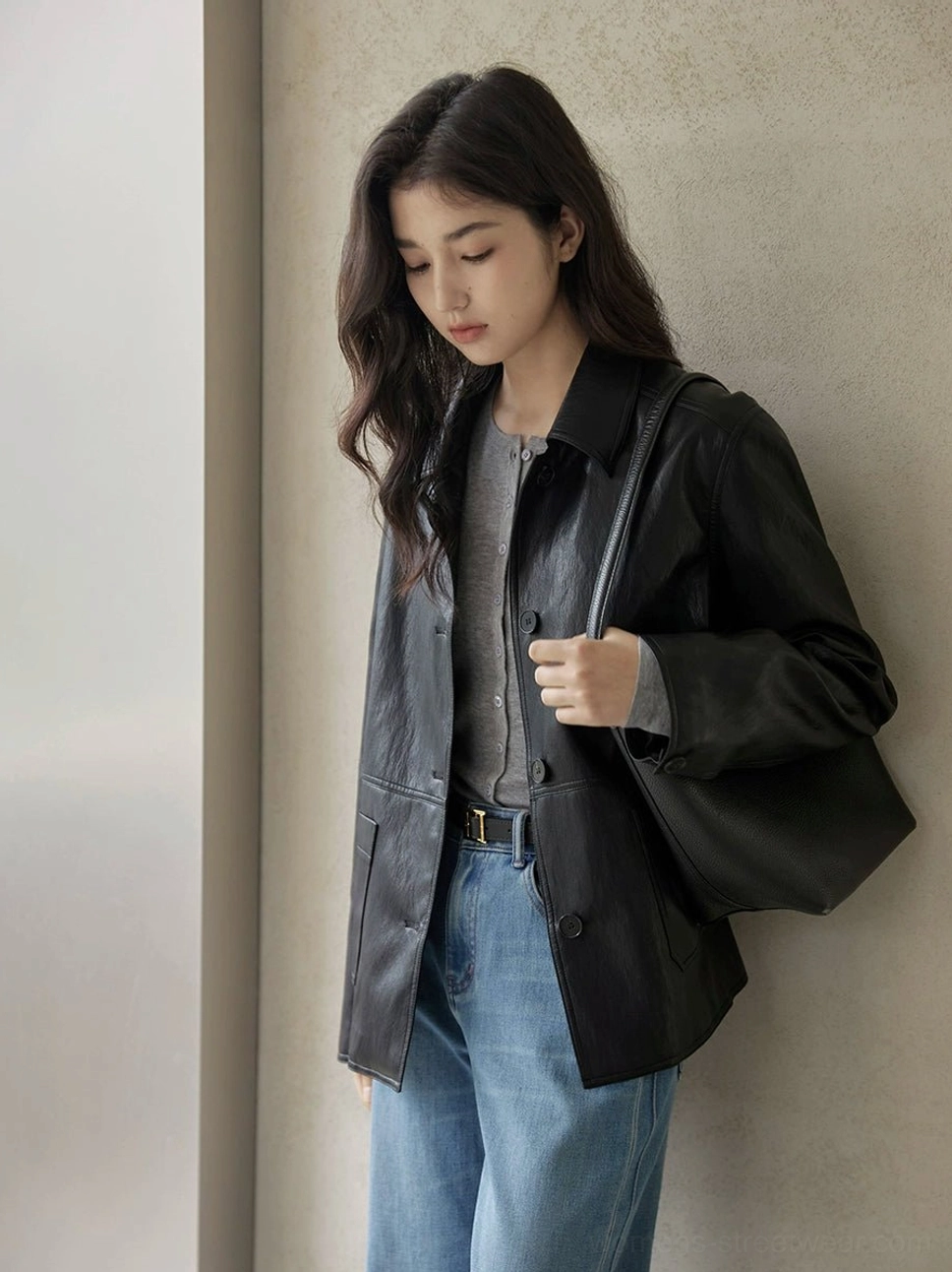 Side three-quarter view of a black short leather jacket with button front and shirt collar styled with jeans