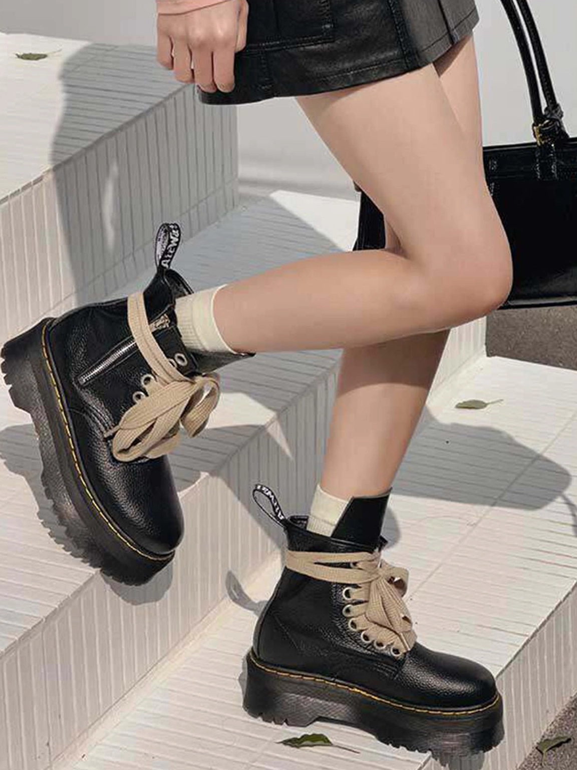 Side view of black ribbon-laced platform combat boots styled with white socks and a black mini skirt for Korean streetwear fashion