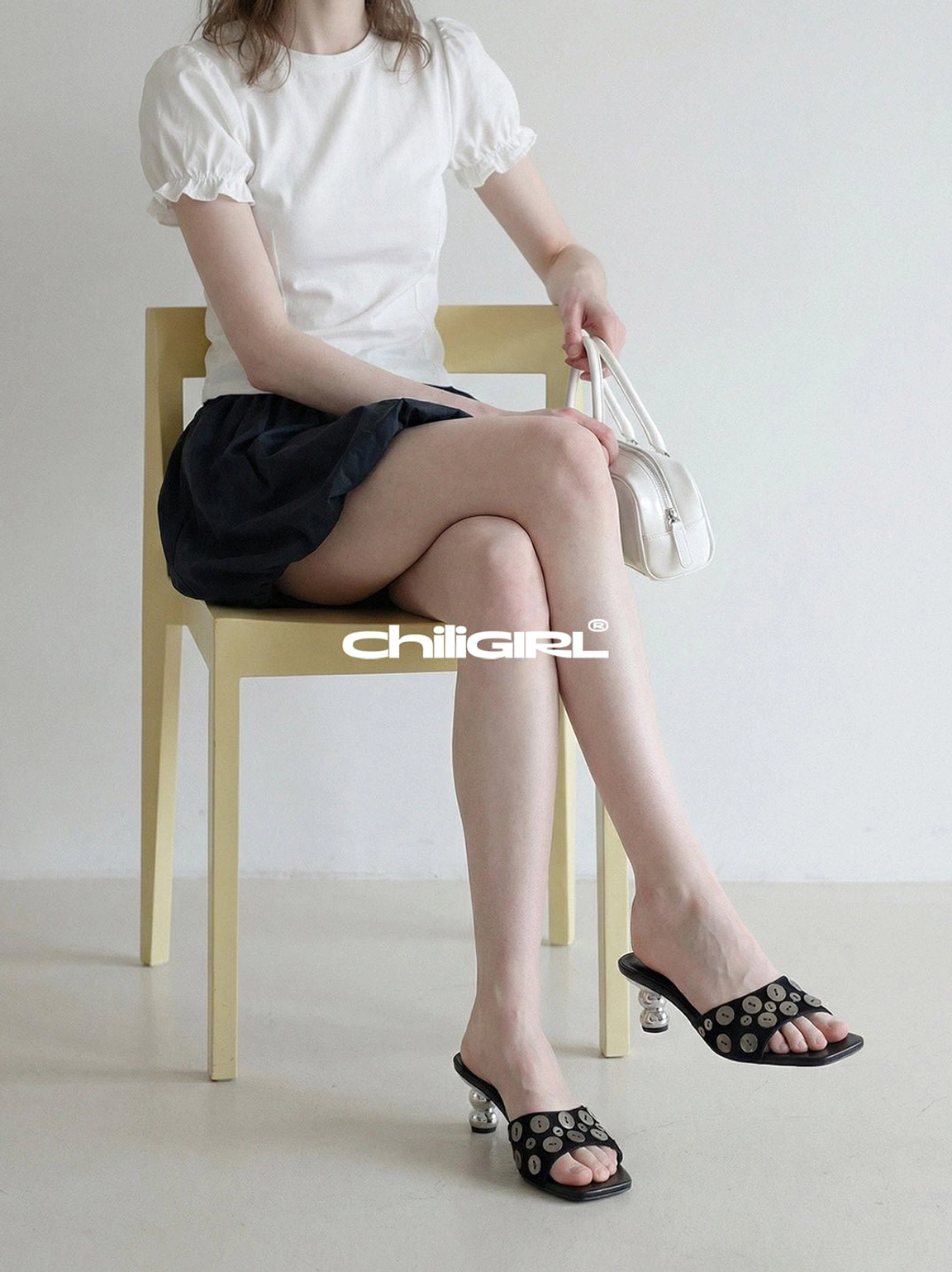 Side profile of black silver disc sculpted heel slides in a feminine Korean streetwear outfit