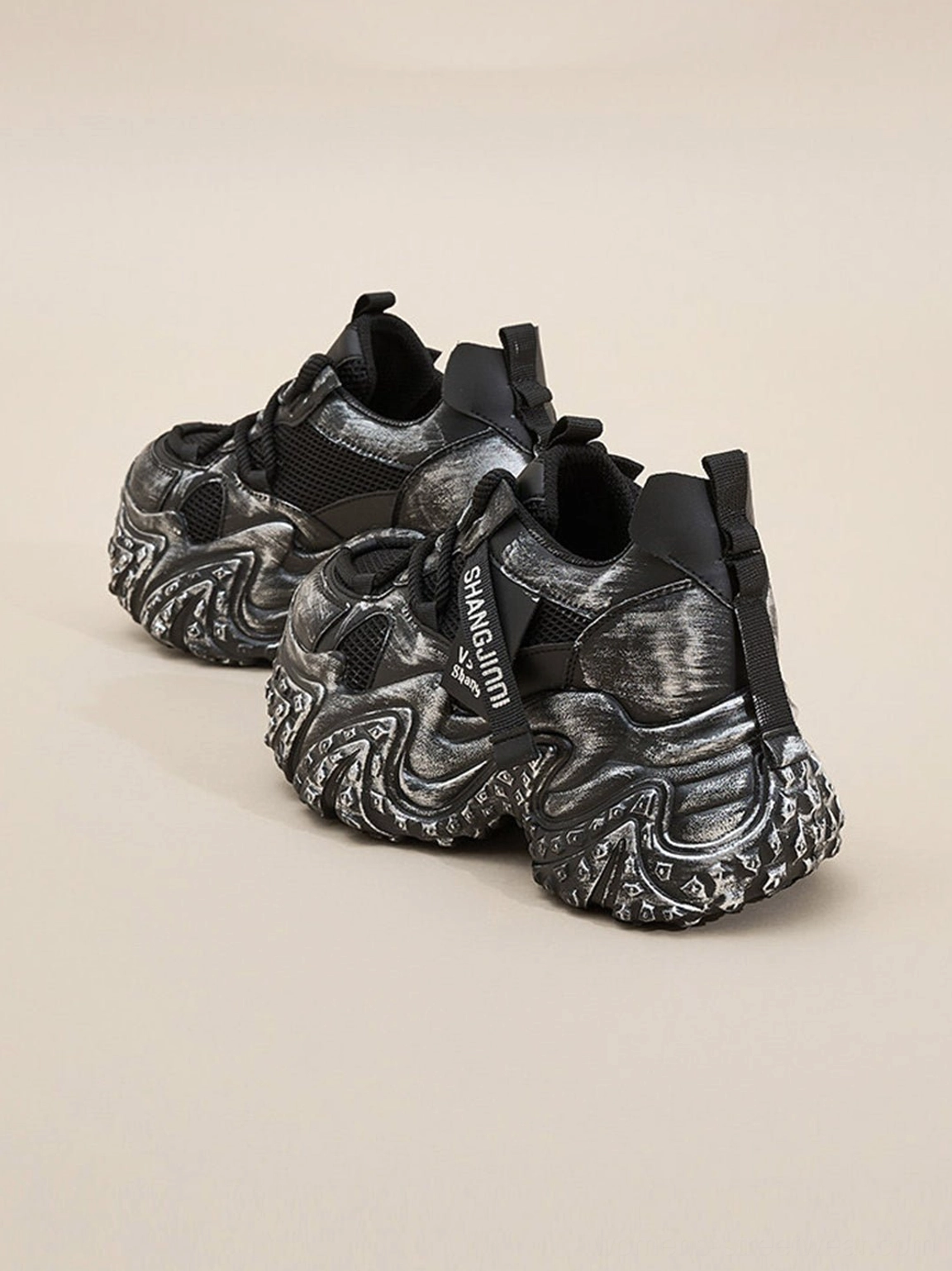 Two pairs of black and silver distressed chunky platform sneakers displayed from top side angle on beige background
