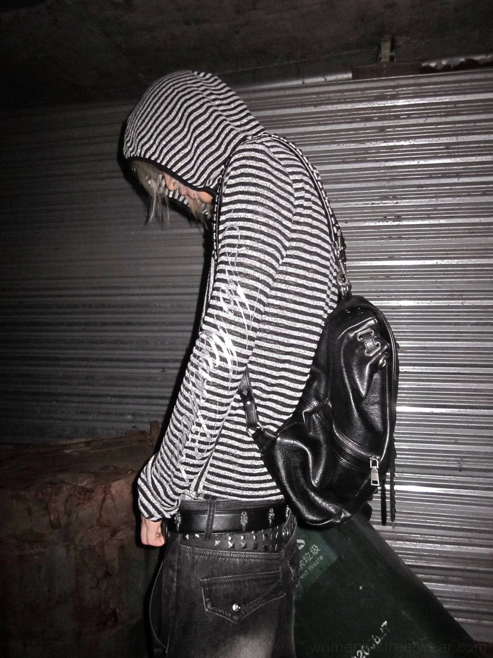 Back view of a black and silver vertical striped hooded cover-up shirt styled with a leather backpack and dark urban streetwear outfit