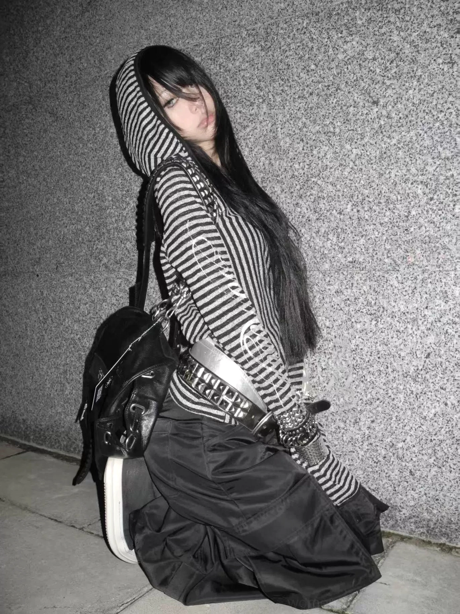 Three-quarter side view of a black and silver striped long-sleeve hooded shirt styled with cargo pants, a wide belt, and an oversized backpack