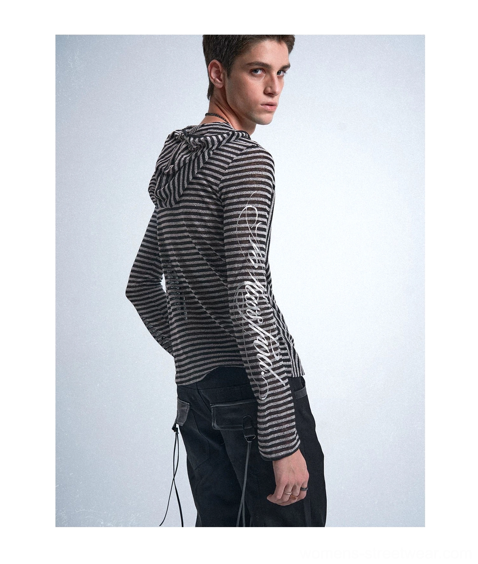 Back full-body view of a black and silver striped zip-up hooded shirt with silver sleeve lettering and dark cargo trousers
