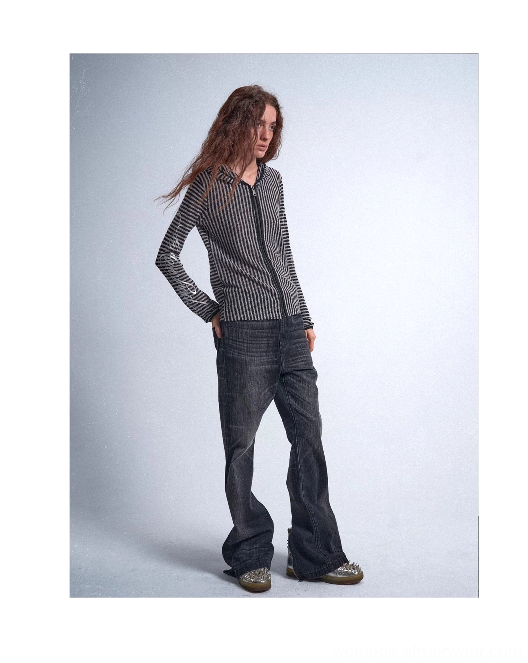 Three-quarter standing view of a black and metallic silver vertical striped hooded cover-up shirt styled with dark flared jeans