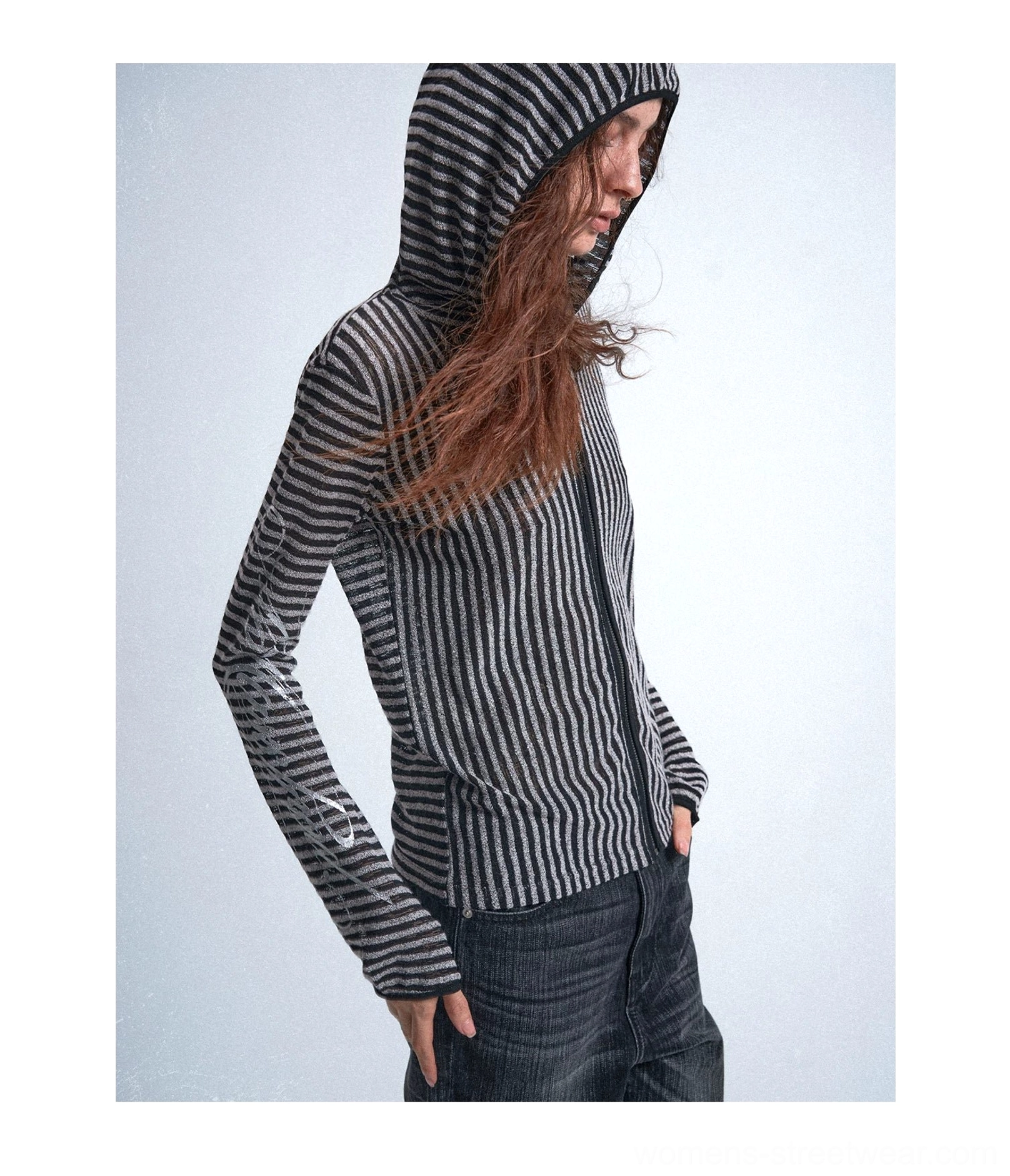 Three-quarter view of a black and silver vertical striped zip-front hooded streetwear shirt worn with dark straight-leg jeans