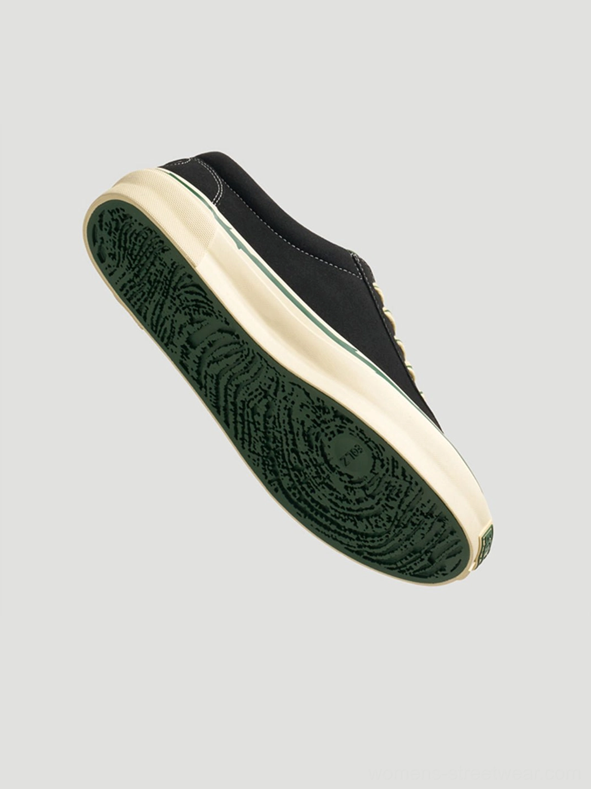 Bottom view of black low-top skate shoes showing textured green rubber outsole, off-white midsole, and detailed tread pattern