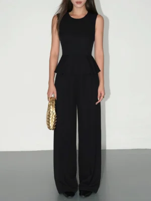 Black sleeveless peplum top and matching high-waist wide-leg trousers styled with a gold woven clutch