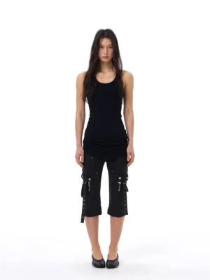 Black slim-fit cargo capri jeans worn with a fitted black tank top and flats, highlighting the cropped length, narrow leg, and punk-inspired side strap pockets