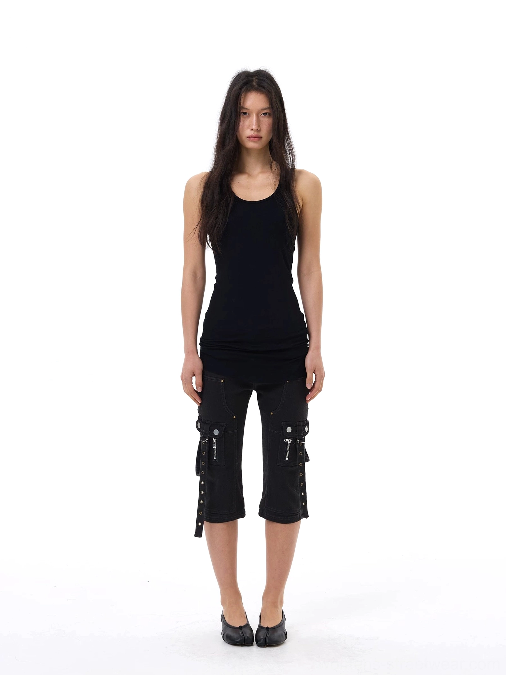 Black slim-fit cargo capri jeans worn with a fitted black tank top and flats, highlighting the cropped length, narrow leg, and punk-inspired side strap pockets